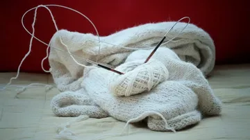 Strickprojekt mit Nadeln auf heller Decke.