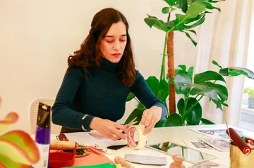 Woman crafting at a table with plants.