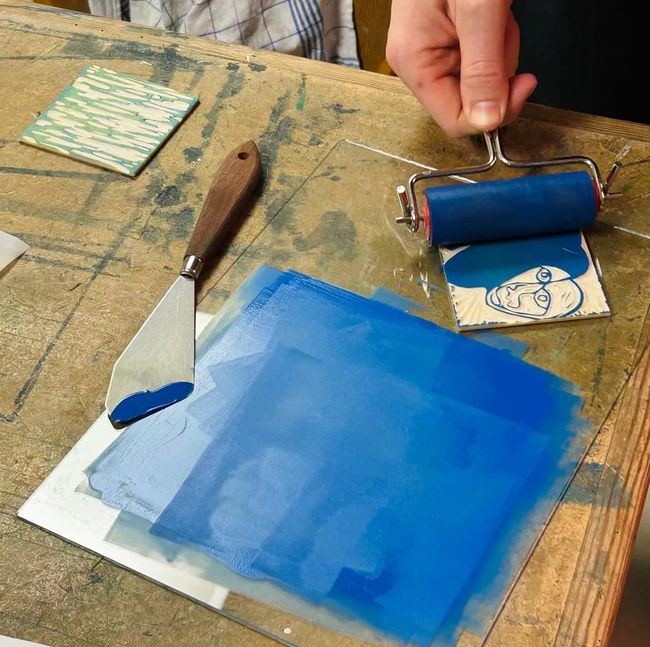 Hand rollt blaue Tinte auf Holzblock.