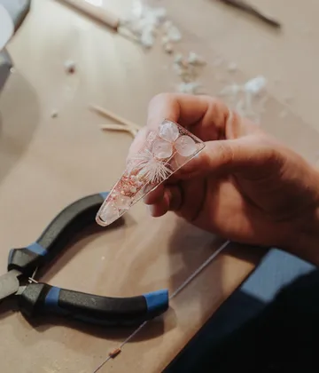 Hand hält Harzanhänger mit getrockneten Blumen.