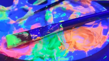 Paintbrushes with neon paint on palette.