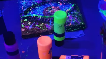 Neon paints and glowing abstract painting under blacklight.