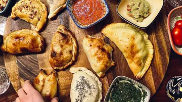 Verschiedene Empanadas und Dips auf Holzbrett.