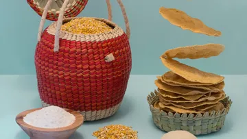 Basket with corn next to flying corn tortillas.