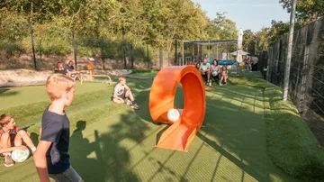 Children playing football golf on grassy course.