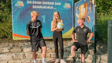 Three individuals smiling near a sports banner.