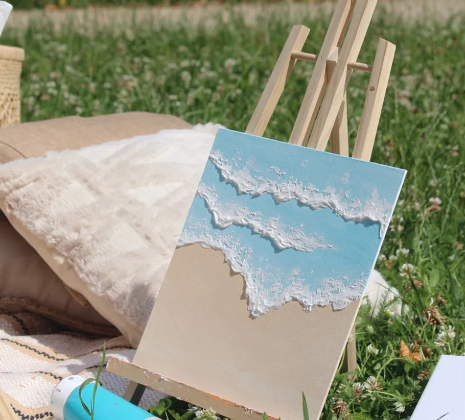 Ocean painting on easel in grassy field.