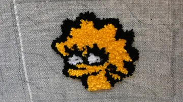 Yellow and black embroidered face on gray fabric.