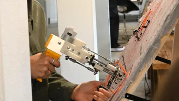 Person benutzt Werkzeug an Tafel in Werkstatt.