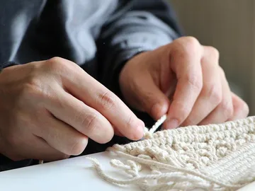 Hands knot wool on a table in a bright room.