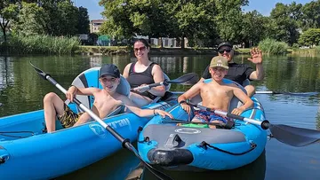 Familie beim Kajakfahren auf ruhigem See unter Bäumen.