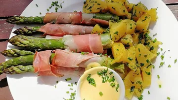 Spargel in Schinken mit Kartoffeln auf Teller.