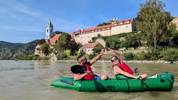 Two people paddle on a river by a castle.