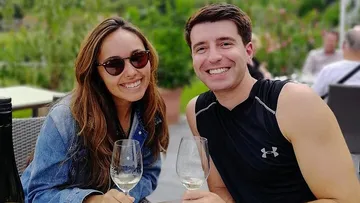 Two people smiling, holding wine glasses, outdoors.