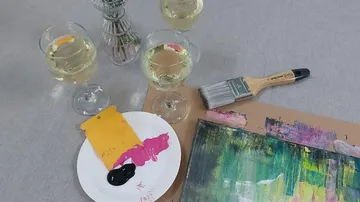 Weingläser mit Malutensilien auf Tisch.