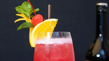 Red cocktail with fruit garnish, black background.