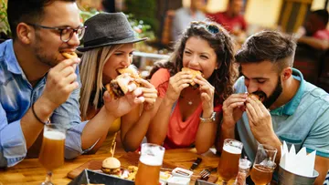 Friends eat burgers at an outdoor cafe.