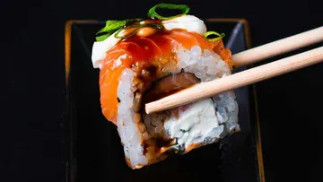 Sushi roll held by chopsticks, black background.