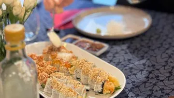 Sushi-Rollen auf Tisch mit essender Person.