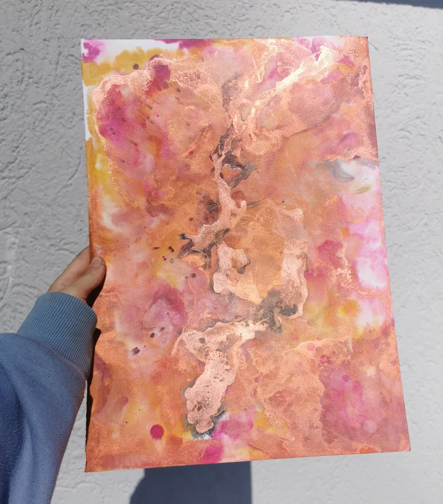 Hand holds abstract painting with pink and gold hues.