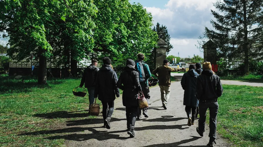 Gruppe geht mit Körben auf Weg unter Bäumen.