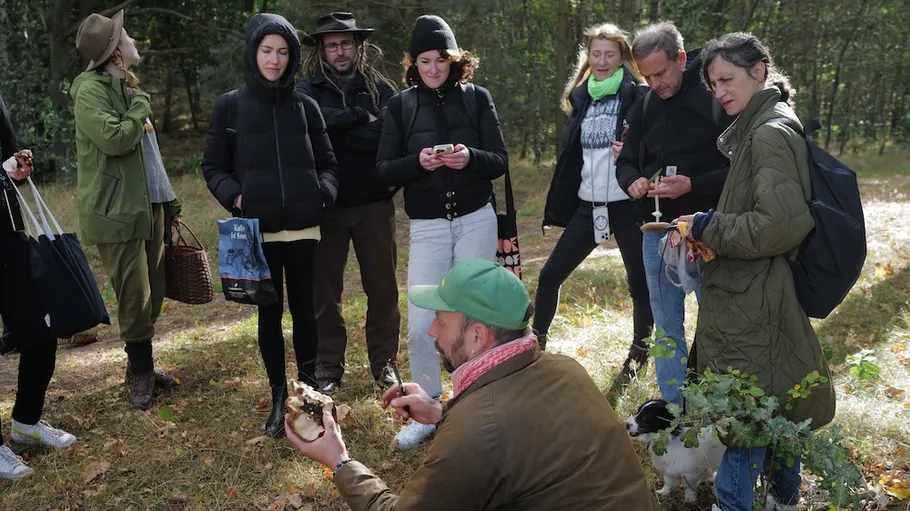 Gruppe versammelt sich um Mann, der Pilze zeigt, draußen.