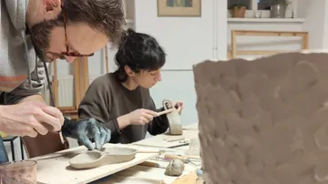 Two people crafting clay objects in a studio.