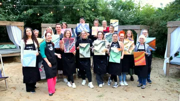 Group of people displaying paintings outdoors.
