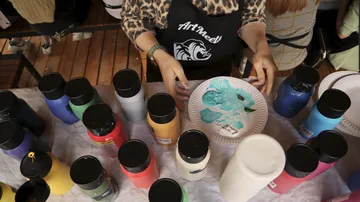 Person preparing paint at table with bottles.