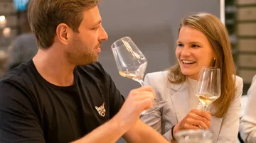 Zwei Personen lächeln mit Weingläsern in der Hand.