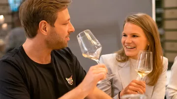 Zwei Personen lachen, halten Weingläser drinnen.