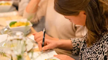 Woman writing at table during a meal.