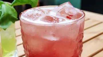 Red cocktail with ice on wooden table.