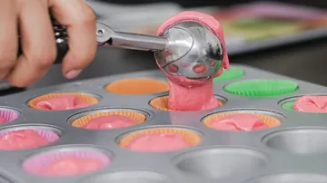 Hand füllt Muffinform mit rosa Teig.