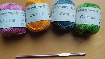 Vier Garnknäuel und Häkelnadel auf Tisch.
