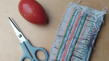 Scissors, pincushion, red egg on wooden table.