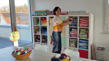 Person organizing fabric shelves in craft room.