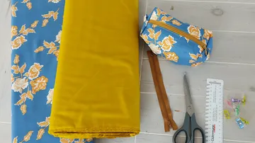 Fabric, scissors, pouch, zipper on wooden table.
