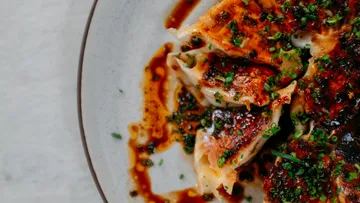 Dumplings mit Soße und Kräutern auf Teller.
