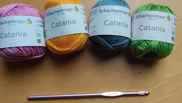 Vier Garnknäuel mit Häkelnadel auf Tisch.