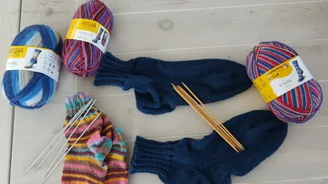 Yarn, knitted socks, and knitting needles on table.