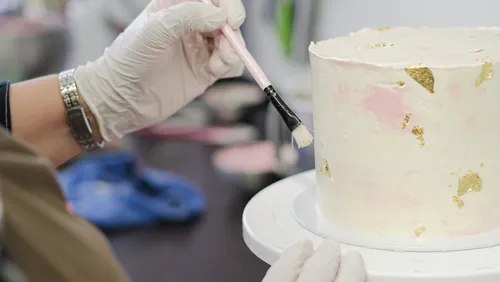Behandschuhte Hand bemalt weißen Kuchen mit Pinsel.