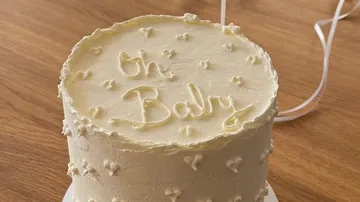 White cake with 'Oh Baby' icing, wooden table.