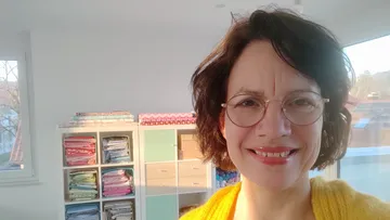 Woman smiling in a bright room, sewing supplies.
