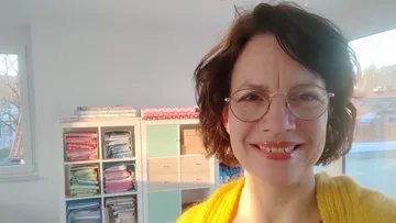 Smiling woman wearing glasses in a fabric-filled room.