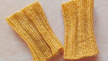 Zwei gelbe gestrickte Handstulpen auf Holzoberfläche.