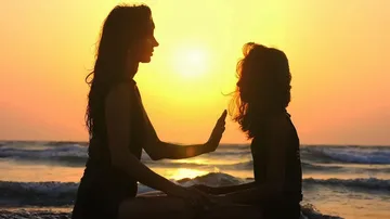 Zwei Personen meditieren am Strand bei Sonnenuntergang.
