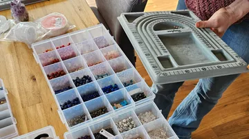 Person holding jewelry tray near bead boxes.