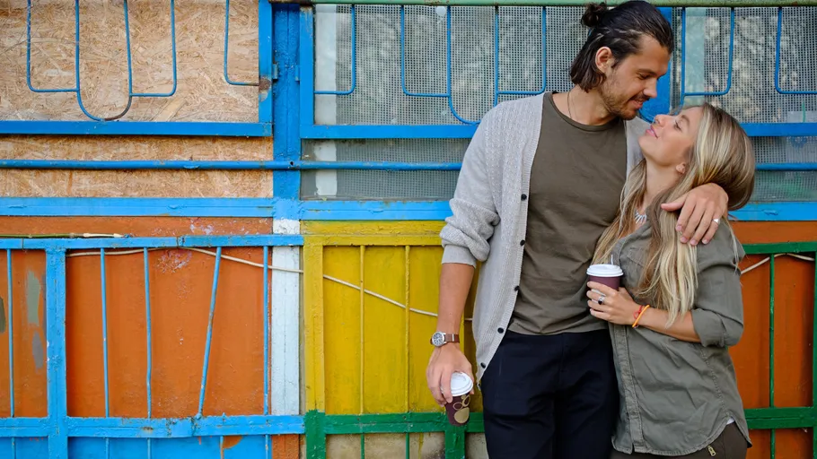 Couple standing, holding coffee, colorful background.