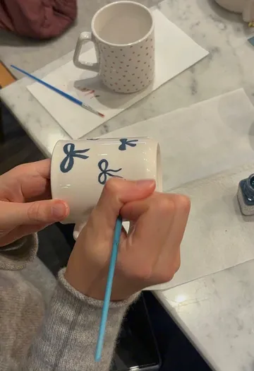Person painting blue designs on a mug.